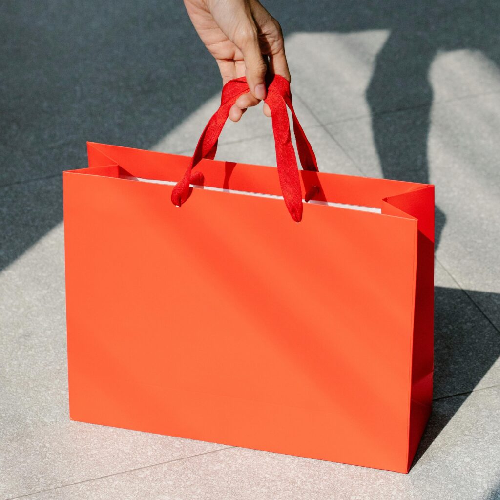 High angle of crop anonymous female buyer taking red paper bag with purchase in sunshine